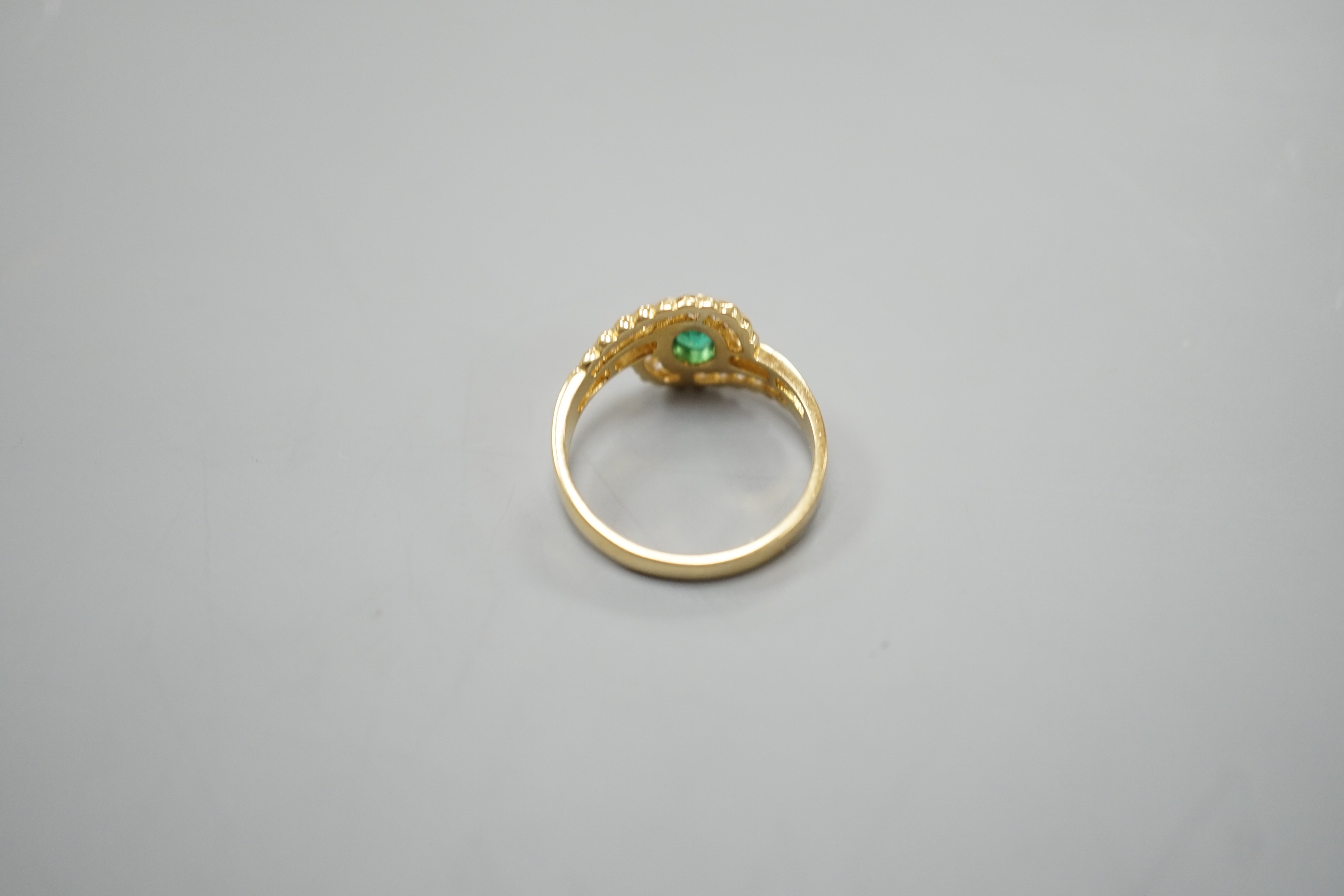 A modern 18ct gold, collet set oval cut emerald and diamond cluster set crossover ring, size N, gross weight 3.5 grams.